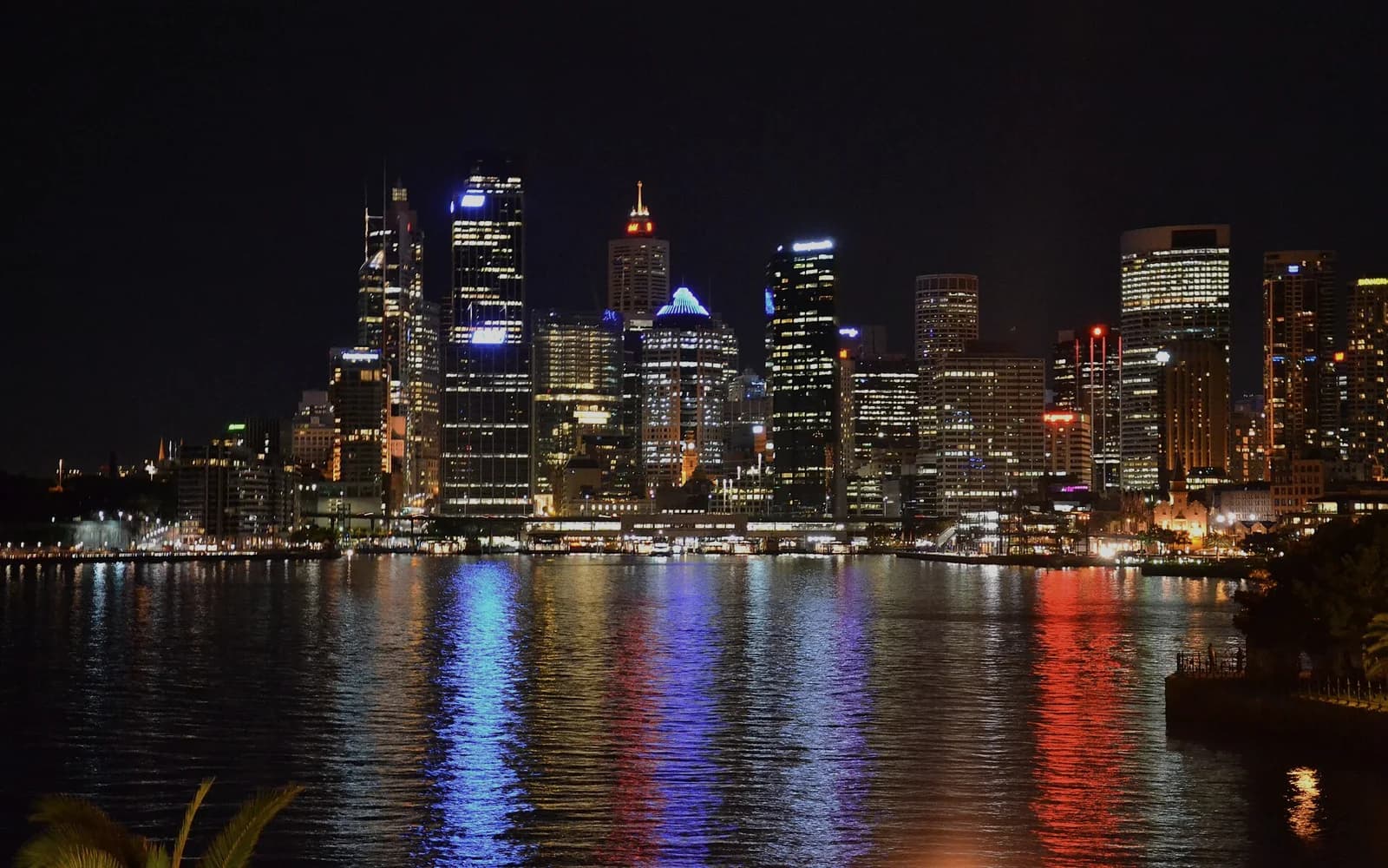 The Sydney city skyline at night seen across Circular Quay, lit towers reflected in the harbour