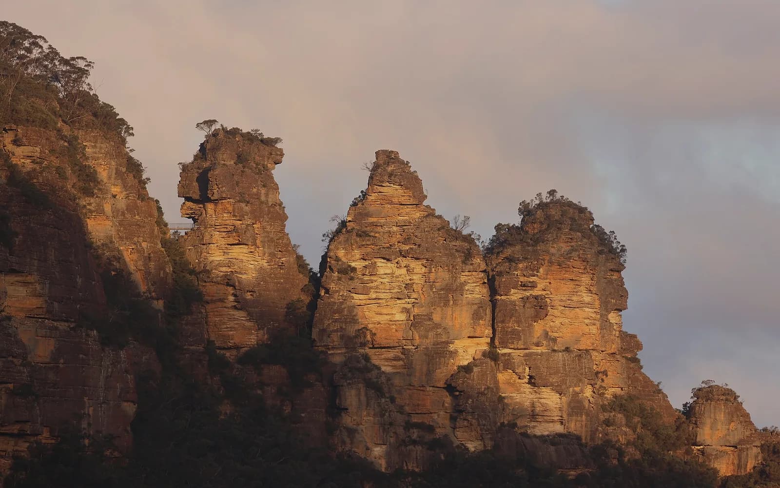 The Three Sisters rock formation at Katoomba, lit warm against the Blue Mountains escarpment